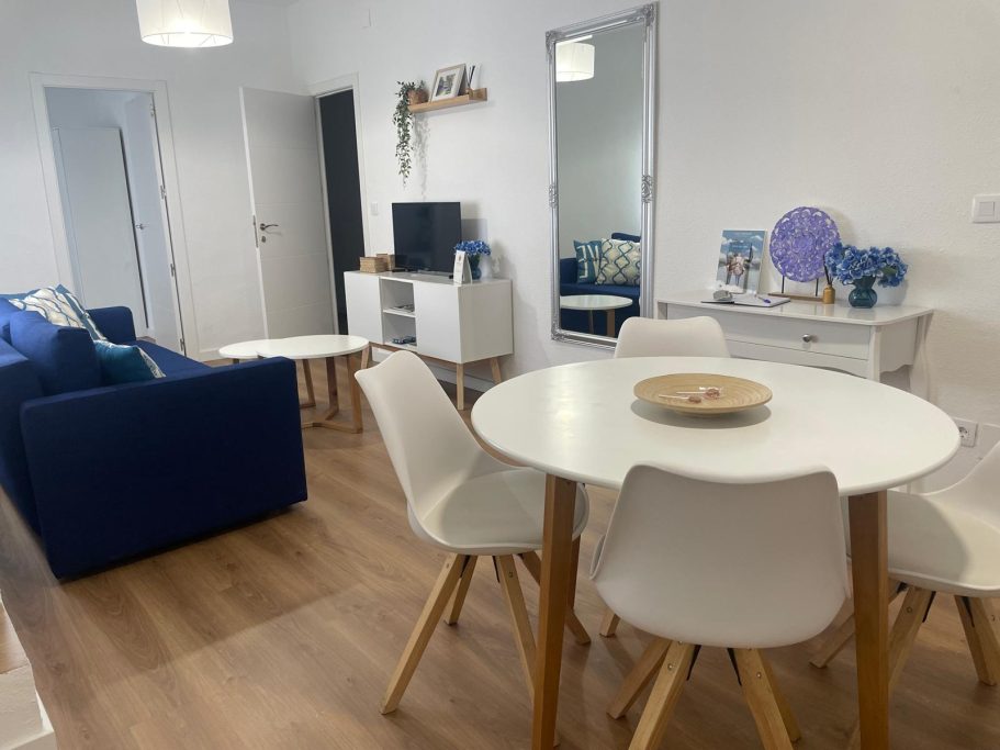 Salón moderno con sofá azul, mesa blanca y sillas, decorado con estilo minimalista.