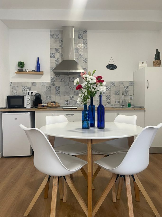 Mesa blanca con flores y botellas azules en una cocina moderna y luminosa.